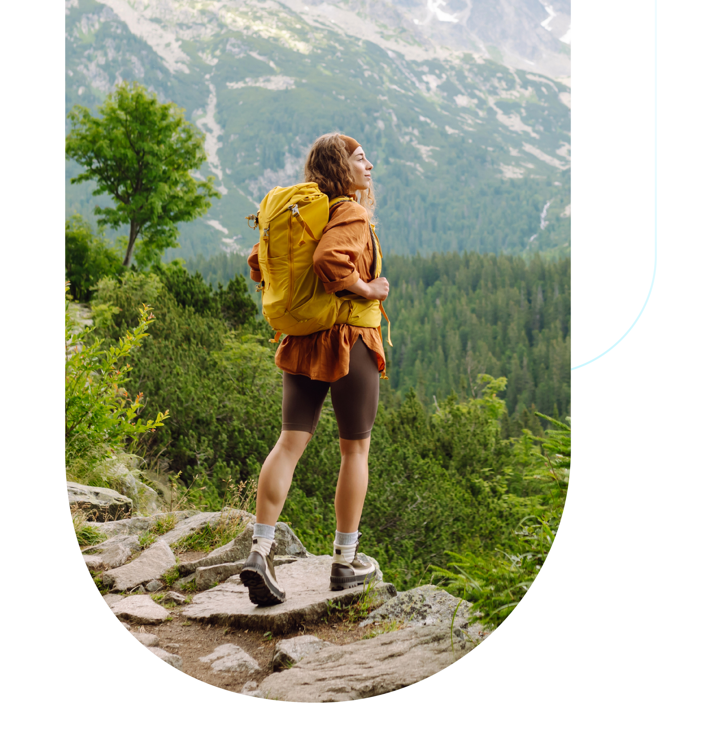 Photo of a young white woman hiking in nature as she looks outward toward a mountain. She's wearing orange themed clothes and hiking gear.